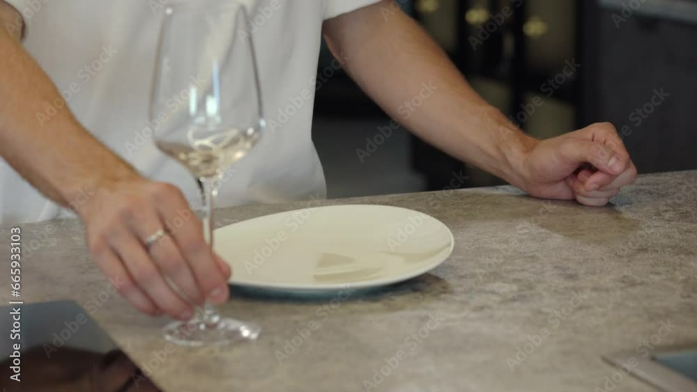 A man puts a white plate and a wine glass on the table A man puts a white plate and a wine glass on the table