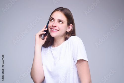 Girl using phone device gadget app isolated over studio background. Woman holding a smartphone, chatting by mobile phone. Girl using phone, studio portrait. Woman makes telephone call on phone. © Volodymyr