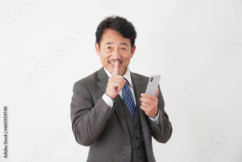スマートフォンを持って内緒のポーズをする中年のビジネスマン 白背景