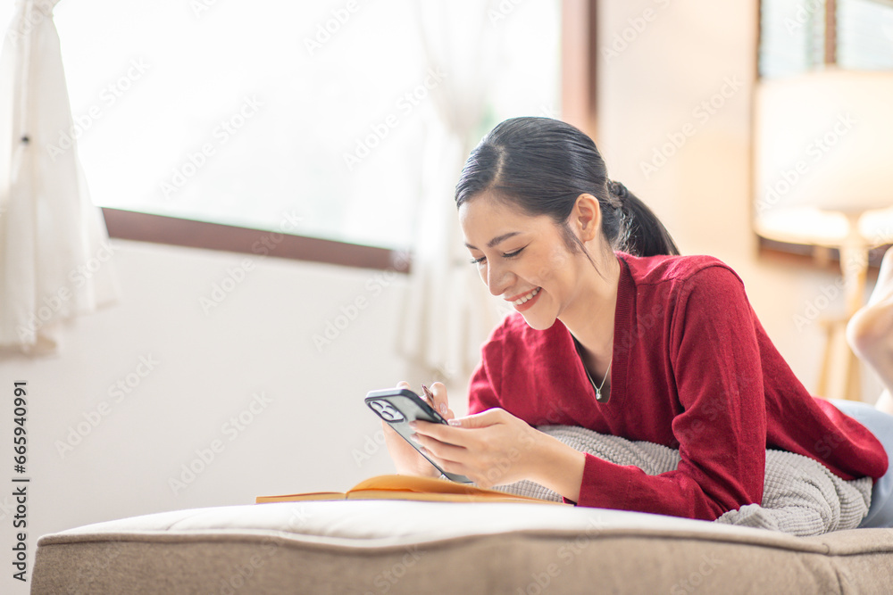 Naklejka premium Happy relaxed young woman sitting on couch using cell phone, smiling lady laughing holding smartphone, looking at cellphone enjoying doing online ecommerce shopping in mobile apps or watching videos.