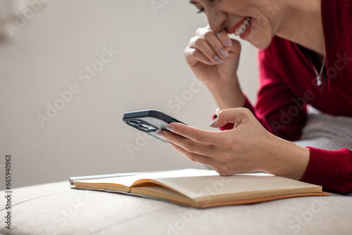 Happy relaxed young woman sitting on couch using cell phone  smiling lady laughing holding smartphone  looking at cellphone enjoying doing online ecommerce shopping in mobile apps or watching videos.