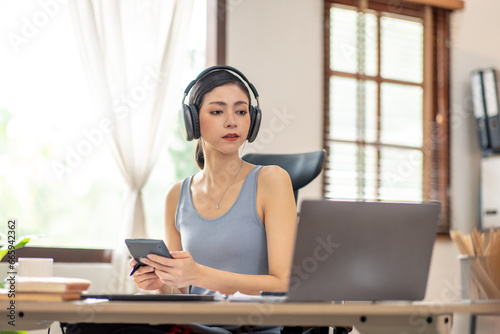 Freelancer Young business asian woman wear wireless headphone and working at home with laptop and papers on desk © David