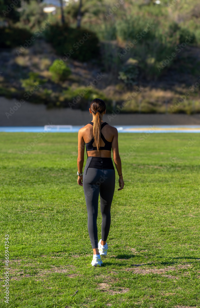 Beautiful young runner girl, on her back, tanned with her long dark hair, walking slowly to warm up before a running race. Illuminated by the light of the evening sun.