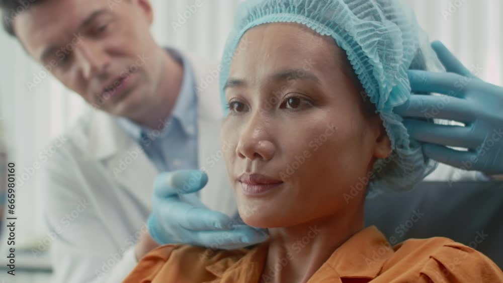 Focus on Asian female patient looking at mirror after procedure of rejuvenation and talking to medical worker Focus on Asian female patient looking at mirror after procedure of rejuvenation and talking to medical worker
