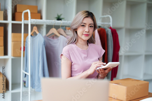 Portrait Of Asian Female Owner Of Fashion Store Checking Stock In Clothing Store With using notebook successful happy smile at small business, sme or ecommerce concepts © Jirapong