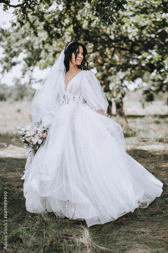 Wedding photography, portrait of a beautiful brunette bride in a nature park with trees.