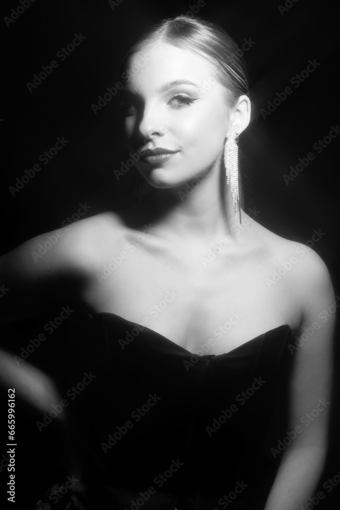 Make-up and fashion concept. Beautiful classic woman portrait. Model with classic hairstyle, fancy earrings, black dress. Shiny star filter applied. Model looking at camera. Black and white image