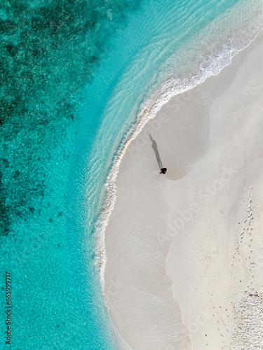 Aerial stock photo of a man standing by the water with turquoise green water captured in higher altitude in the Maldives.
