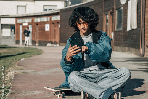 teenager boy playing with phone sitting on skateboard on the street