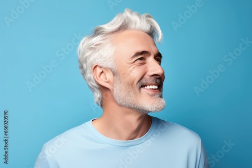 Middle-aged caucasian man on blue backdrop looks aside smiling, cheerful and pleasant.