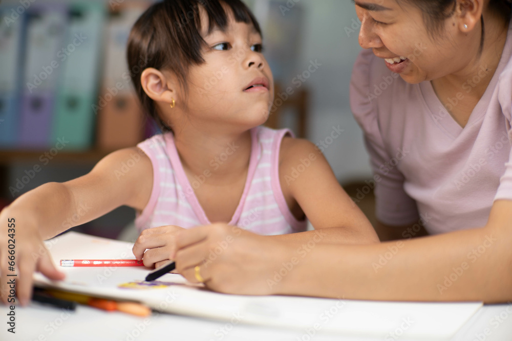 Mother and daughter drawing together with crayons. Adult woman helps girl study or draw together at home in living room. Happy family. Mother and daughter drawing together with crayons. Adult woman helps girl study or draw together at home in living room. Happy family.