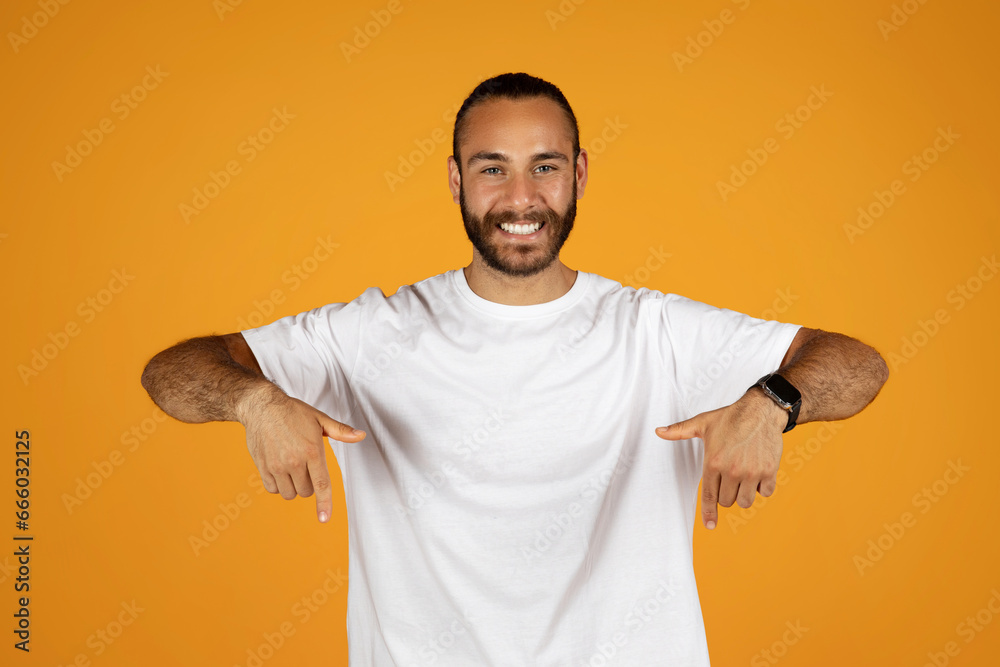 Glad millennial european guy in white t-shirt point finger down at free space, recommends ad and offer Glad millennial european guy in white t-shirt point finger down at free space, recommends ad and offer