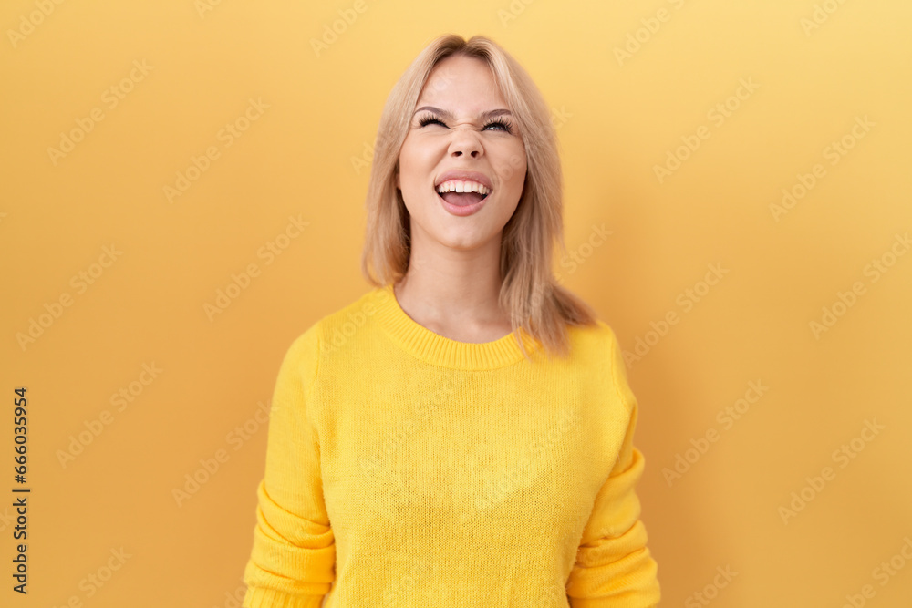 Young caucasian woman wearing yellow sweater angry and mad screaming frustrated and furious, shouting with anger. rage and aggressive concept. Young caucasian woman wearing yellow sweater angry and mad screaming frustrated and furious, shouting with anger. rage and aggressive concept.