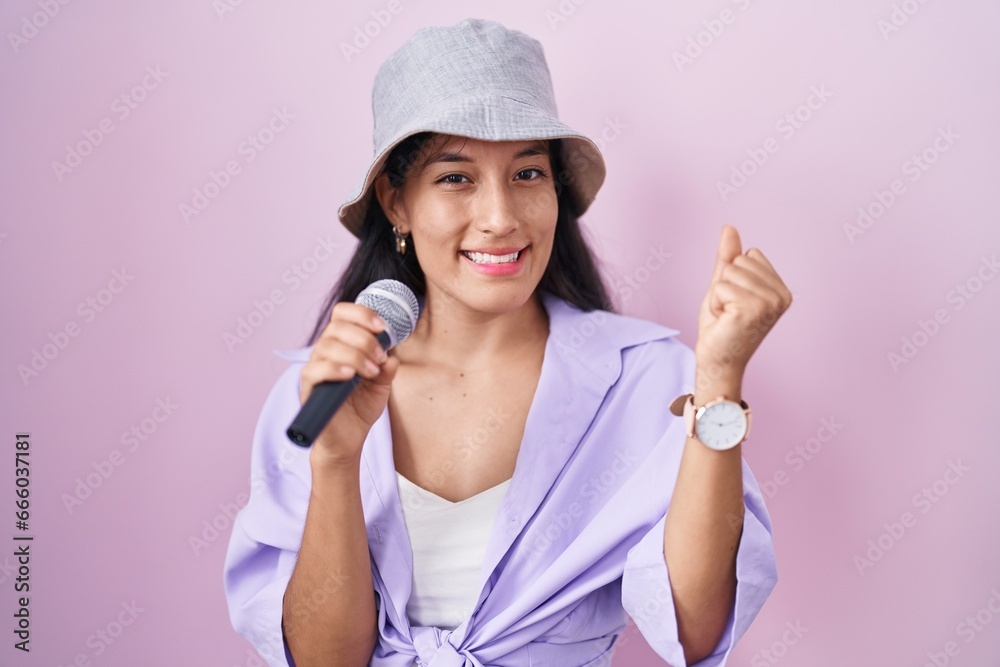 Young hispanic woman singing song using microphone over pink background screaming proud, celebrating victory and success very excited with raised arms Young hispanic woman singing song using microphone over pink background screaming proud, celebrating victory and success very excited with raised arms