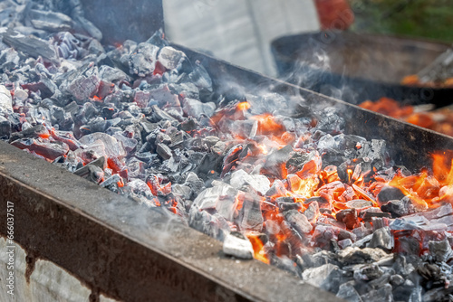 Fire and smoldering coals inside a metal grill for frying meat or vegetables outdoors. Preparing for a picnic