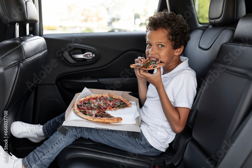 Hungry african american boy eating pizza while riding car
