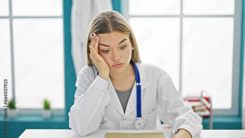 Young blonde woman doctor sitting on table tired at clinic Young blonde woman doctor sitting on table tired at clinic