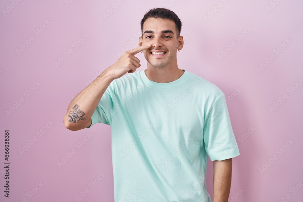 Handsome hispanic man standing over pink background pointing with hand finger to face and nose, smiling cheerful. beauty concept Handsome hispanic man standing over pink background pointing with hand finger to face and nose, smiling cheerful. beauty concept