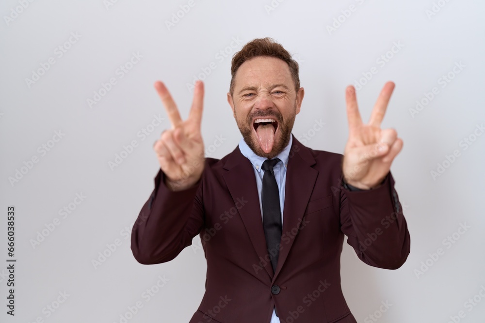 Middle age business man with beard wearing suit and tie smiling with tongue out showing fingers of both hands doing victory sign. number two. Middle age business man with beard wearing suit and tie smiling with tongue out showing fingers of both hands doing victory sign. number two.