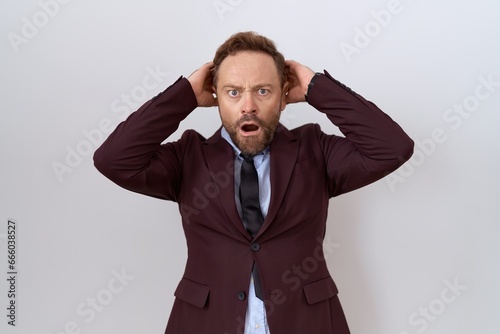 Middle age business man with beard wearing suit and tie crazy and scared with hands on head, afraid and surprised of shock with open mouth