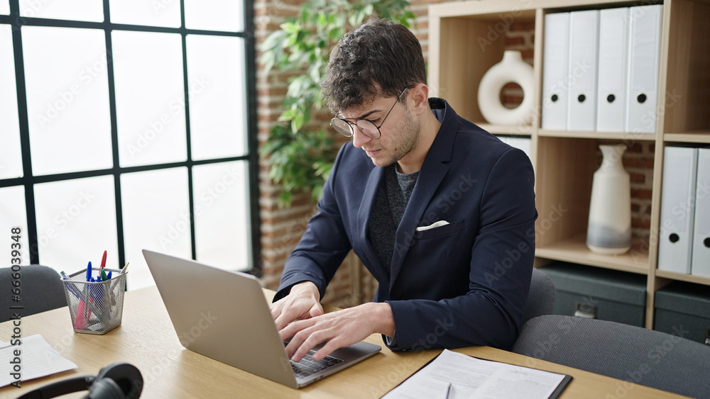 Young hispanic man business worker using laptop with serious face at office