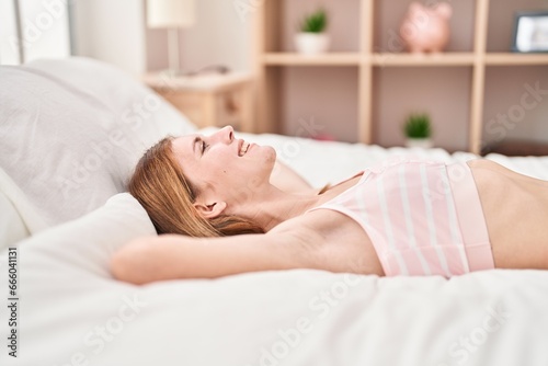 Young blonde woman lying on bed relaxed with hands on head at bedroom