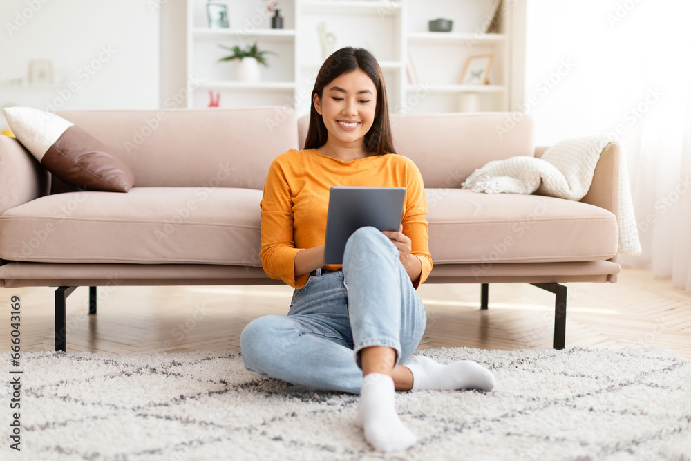 Fototapeta premium Happy asian woman sitting on floor, using digital tablet