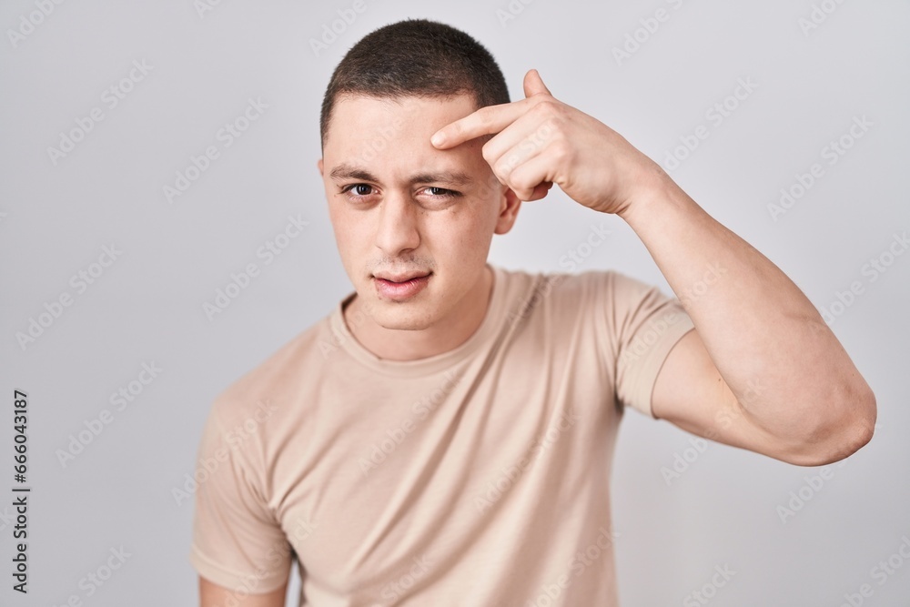 Young man standing over isolated background pointing unhappy to pimple on forehead, ugly infection of blackhead. acne and skin problem Young man standing over isolated background pointing unhappy to pimple on forehead, ugly infection of blackhead. acne and skin problem