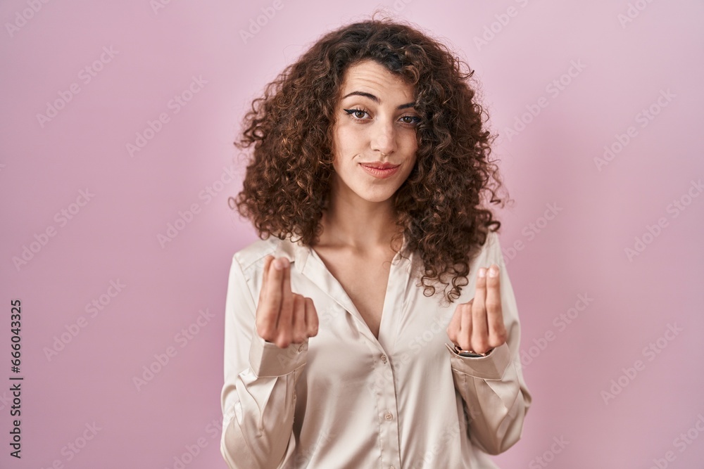Hispanic woman with curly hair standing over pink background doing money gesture with hands, asking for salary payment, millionaire business Hispanic woman with curly hair standing over pink background doing money gesture with hands, asking for salary payment, millionaire business