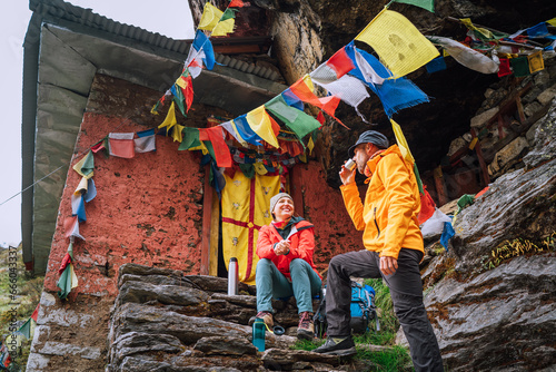 Canvas Print Chatting smiling Backpackers Couple tea break at small sacred Buddhist monastery decorated multicolored Tibetan prayer flags with mantras