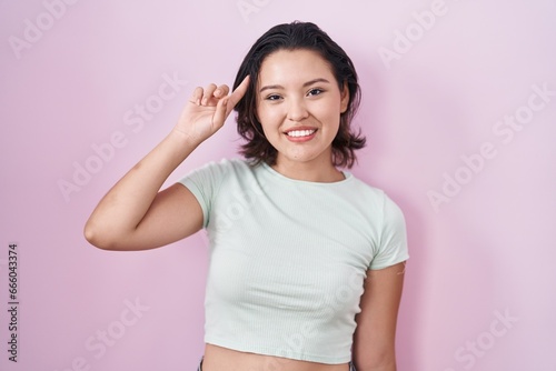 Hispanic young woman standing over pink background smiling pointing to head with one finger  great idea or thought  good memory