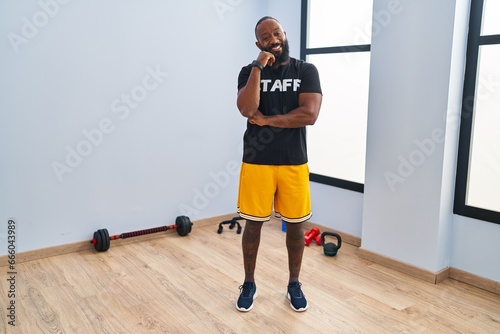 African american man working at fitness gym smiling looking confident at the camera with crossed arms and hand on chin. thinking positive.