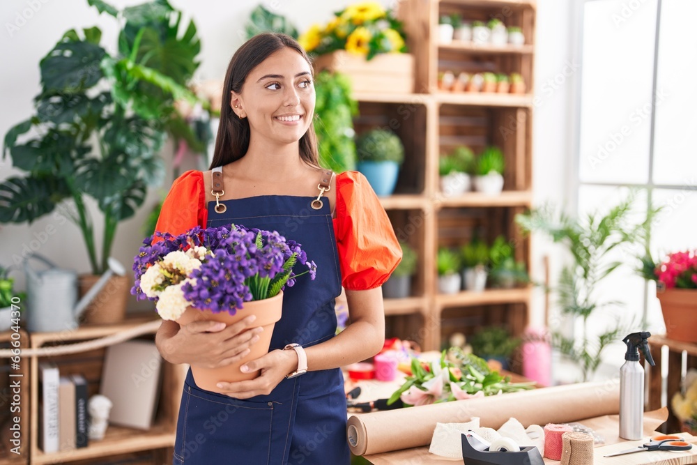 Young beautiful hispanic woman florist smiling confident holding plant at florist