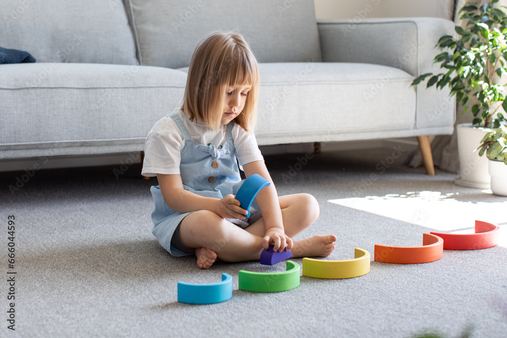 A cute girl is playing an educational game with a wooden rainbow. child development A cute girl is playing an educational game with a wooden rainbow. child development