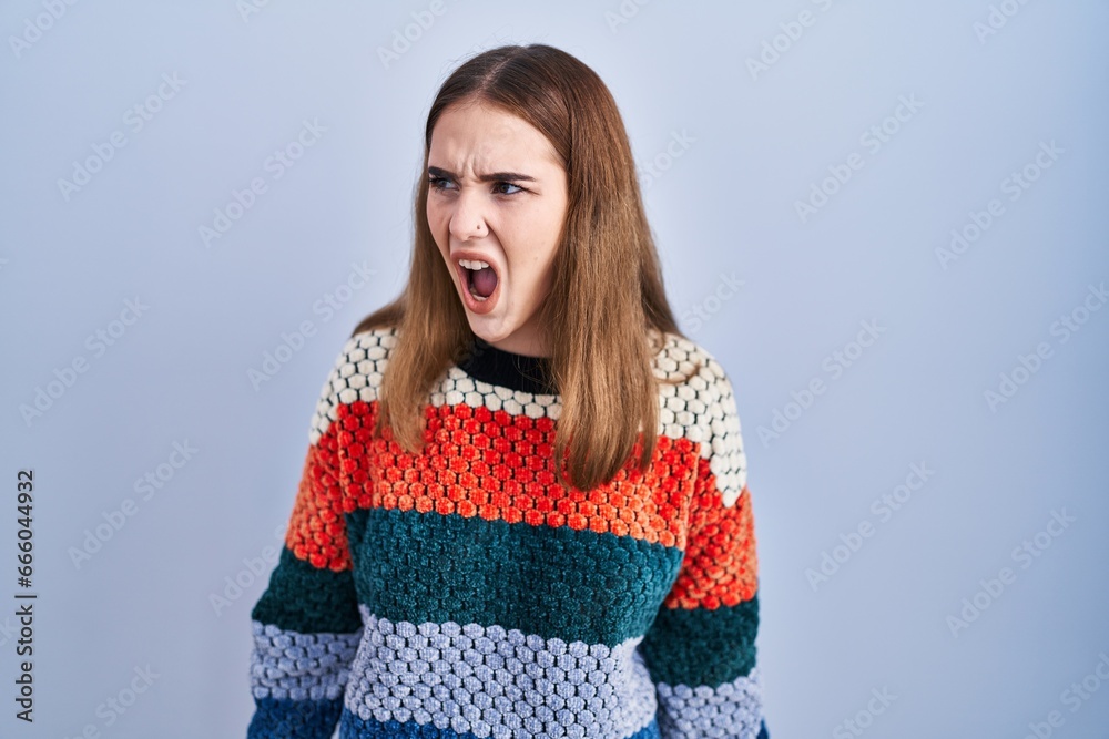 Young hispanic girl standing over blue background angry and mad screaming frustrated and furious, shouting with anger. rage and aggressive concept. Young hispanic girl standing over blue background angry and mad screaming frustrated and furious, shouting with anger. rage and aggressive concept.