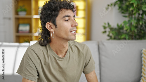 Young hispanic man sitting on sofa speaking at home