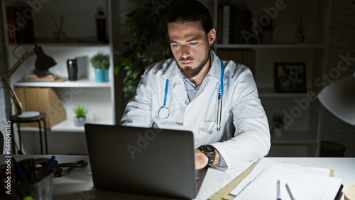 Young hispanic man doctor using laptop working at the clinic