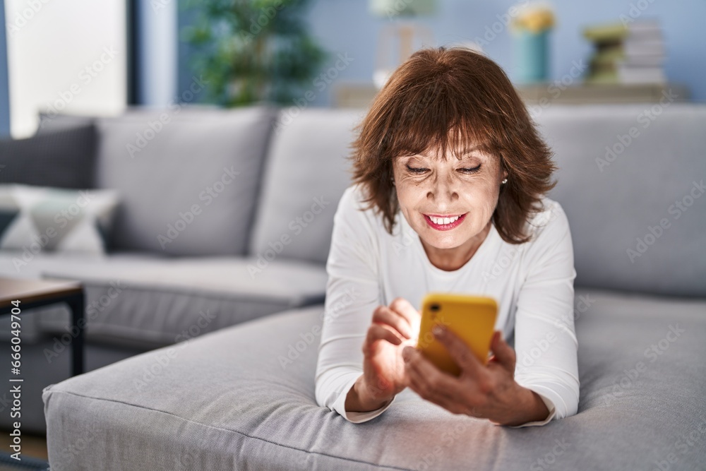 Middle age woman using smartphone lying on sofa at home Middle age woman using smartphone lying on sofa at home
