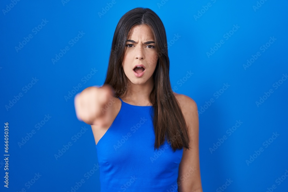 Hispanic woman standing over blue background pointing displeased and frustrated to the camera, angry and furious with you Hispanic woman standing over blue background pointing displeased and frustrated to the camera, angry and furious with you