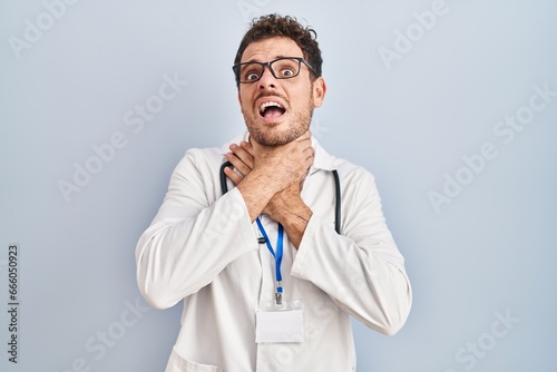 Young hispanic man wearing doctor uniform and stethoscope shouting and suffocate because painful strangle. health problem. asphyxiate and suicide concept.