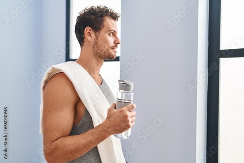 Young hispanic man wearing sportswear drinking water looking to side, relax profile pose with natural face and confident smile.