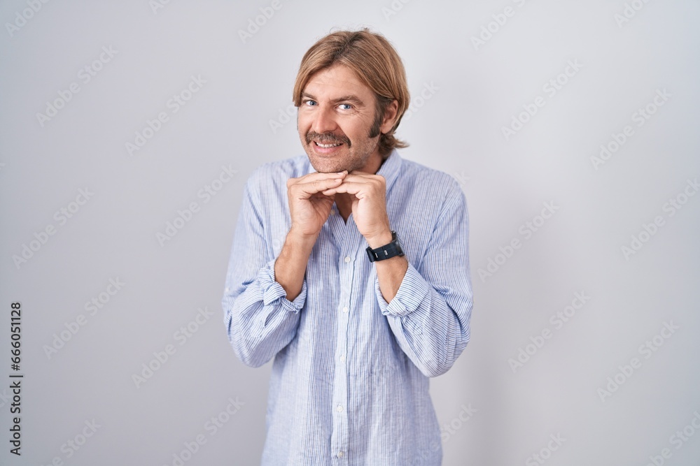 Caucasian man with mustache standing over white background laughing nervous and excited with hands on chin looking to the side Caucasian man with mustache standing over white background laughing nervous and excited with hands on chin looking to the side