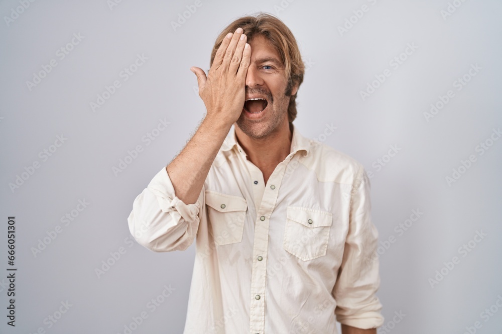 Middle age man standing over isolated background covering one eye with hand, confident smile on face and surprise emotion. Middle age man standing over isolated background covering one eye with hand, confident smile on face and surprise emotion.
