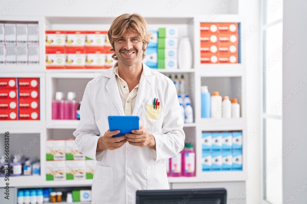 Young man pharmacist smiling confident using touchpad at pharmacy