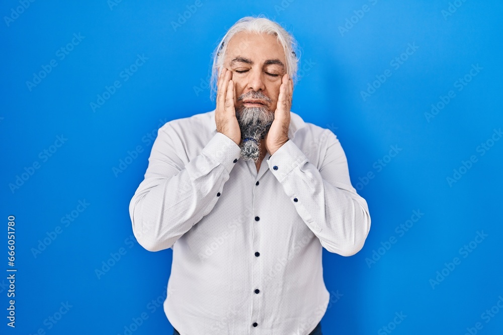Middle age man with grey hair standing over blue background tired hands covering face, depression and sadness, upset and irritated for problem Middle age man with grey hair standing over blue background tired hands covering face, depression and sadness, upset and irritated for problem