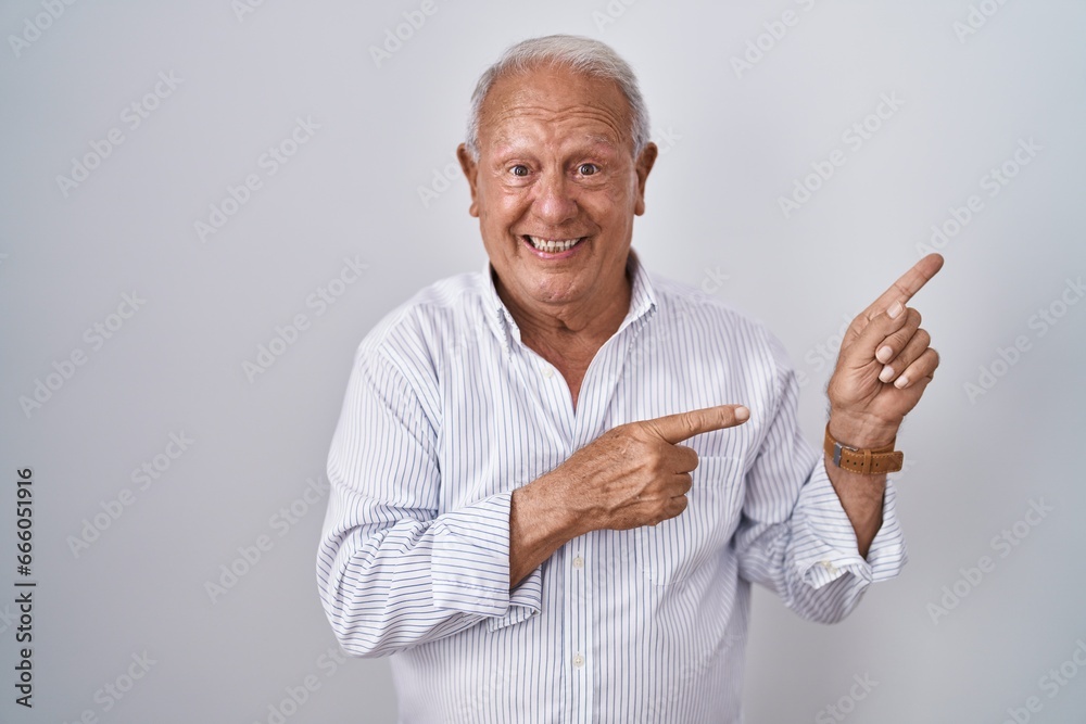 Senior man with grey hair standing over isolated background smiling and looking at the camera pointing with two hands and fingers to the side. Senior man with grey hair standing over isolated background smiling and looking at the camera pointing with two hands and fingers to the side.