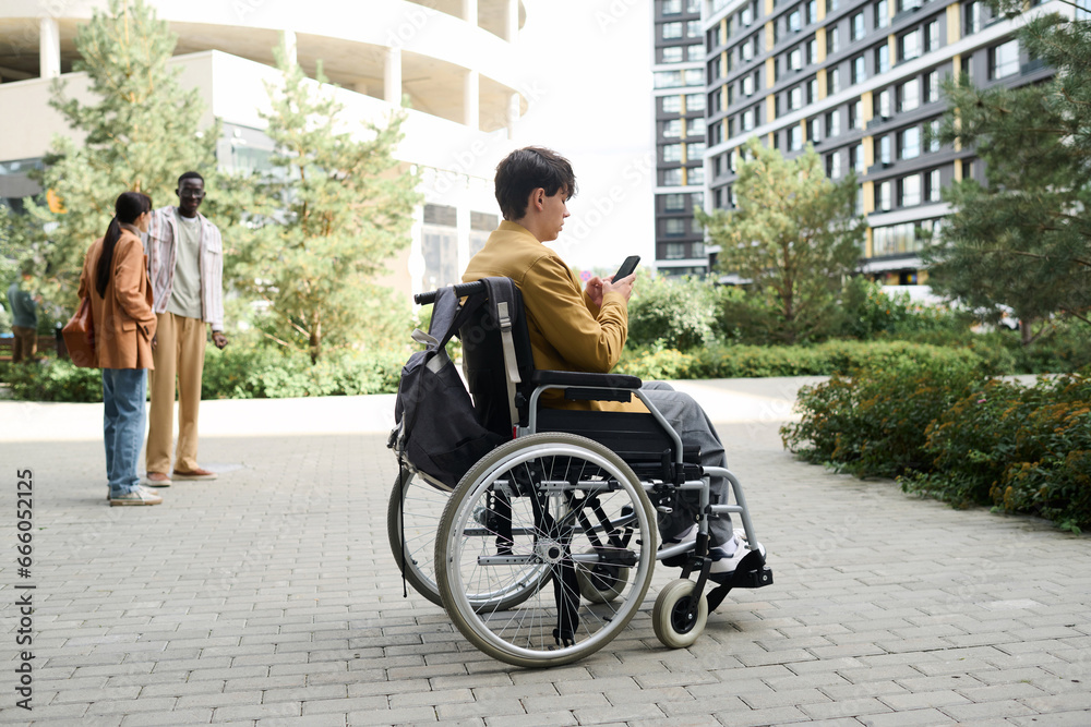 Obraz premium Man sitting in wheelchair and using smartphone during his walk in the city
