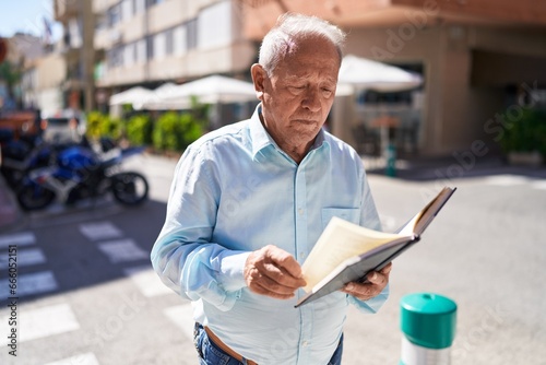 Middle age grey-haired man reading book at street