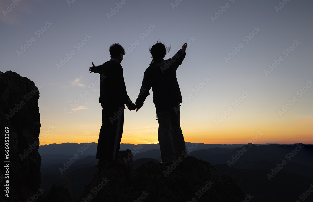 Silhouettes of a Christian man and woman spreading their arms to ask for blessings on a mountain. Together for recovery, providing emotional support. Praying for love and faith in religion.