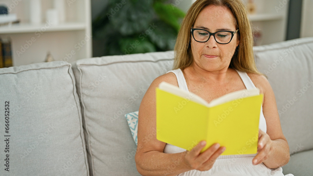 Middle age hispanic woman reading book sitting on sofa at home Middle age hispanic woman reading book sitting on sofa at home